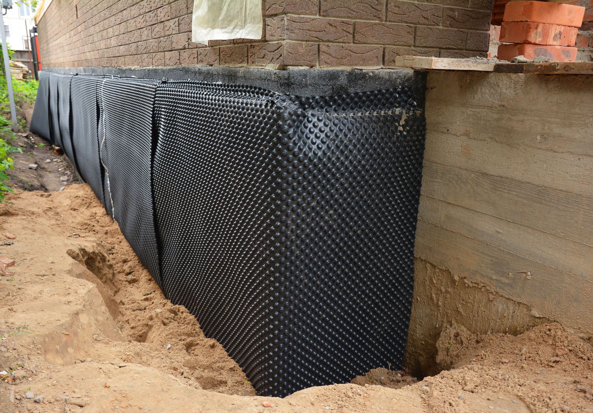 Black waterproofing membrane wrapped around a basement foundation wall in an excavated trench. Black waterproofing membrane wrapped around a basement foundation wall in an excavated trench.