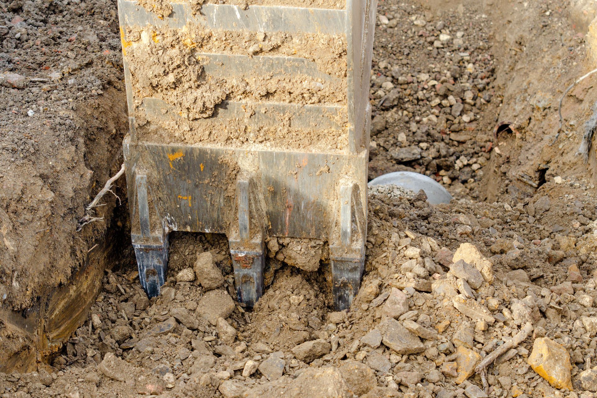 Excavator bucket digging into rocky soil at a construction site