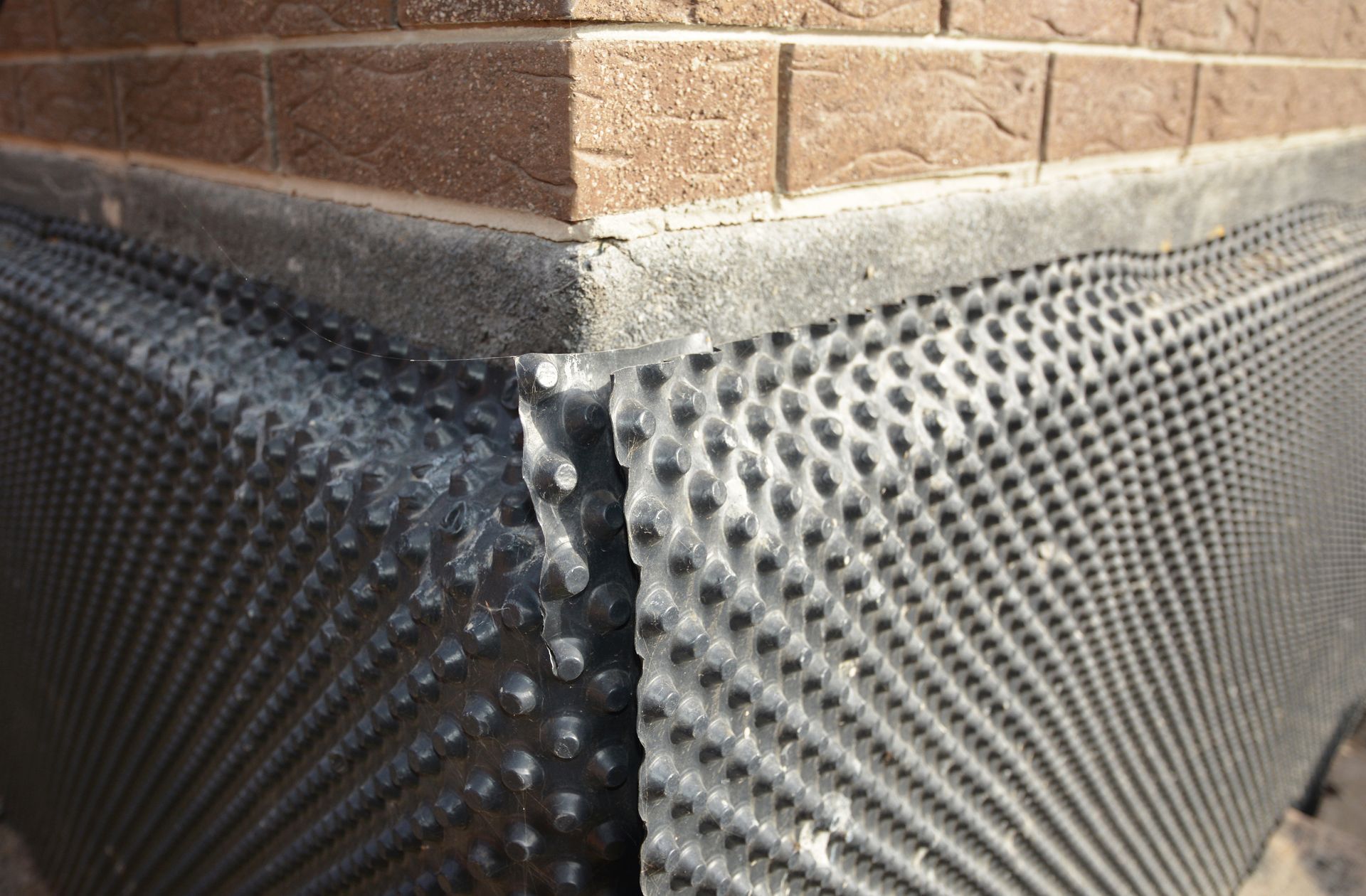 Black dimpled foundation waterproofing membrane on a brick building corner outdoors Black dimpled foundation waterproofing membrane on a brick building corner outdoors