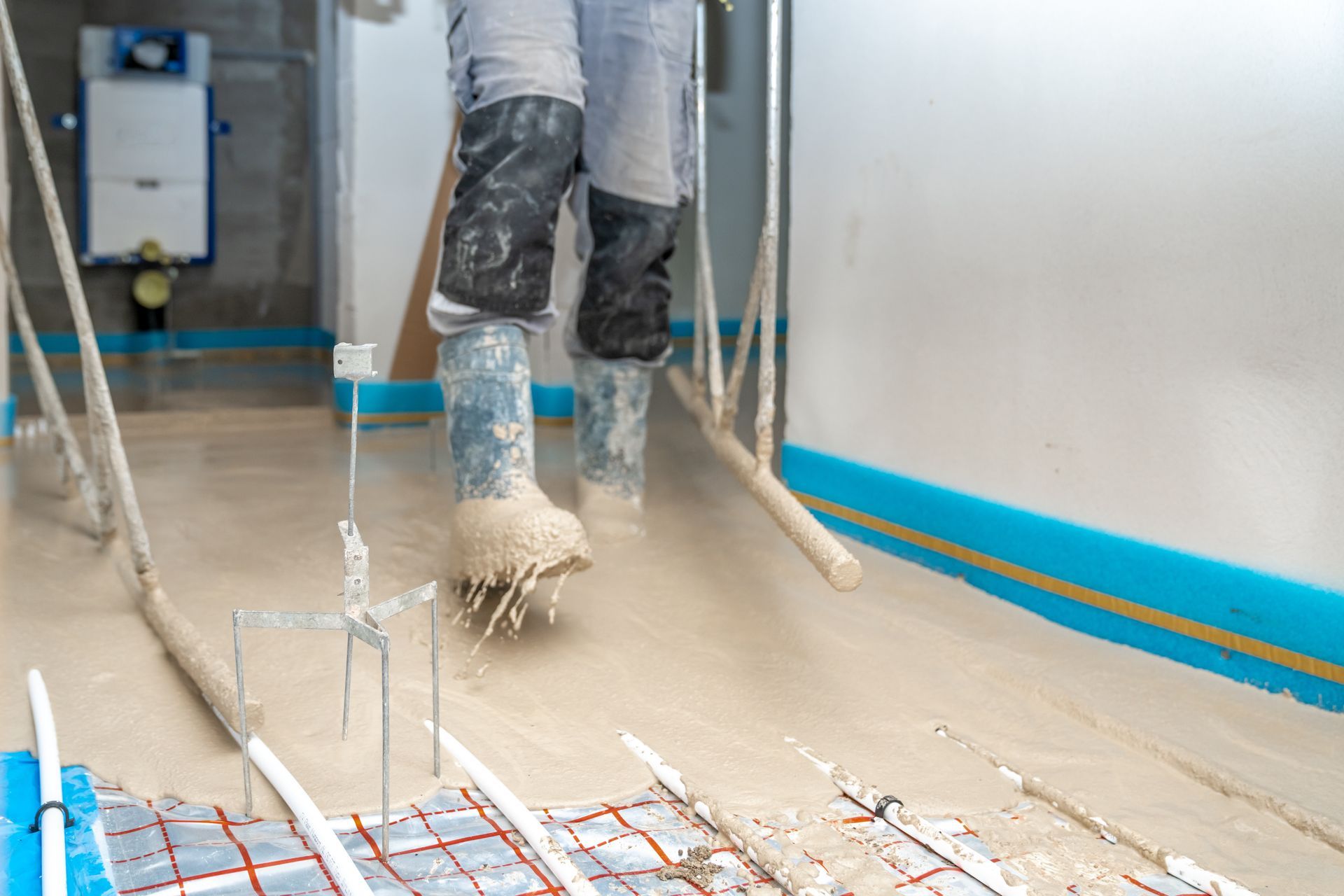 Worker spreading wet concrete over floor with a squeegee in an indoor construction area Worker spreading wet concrete over floor with a squeegee in an indoor construction area