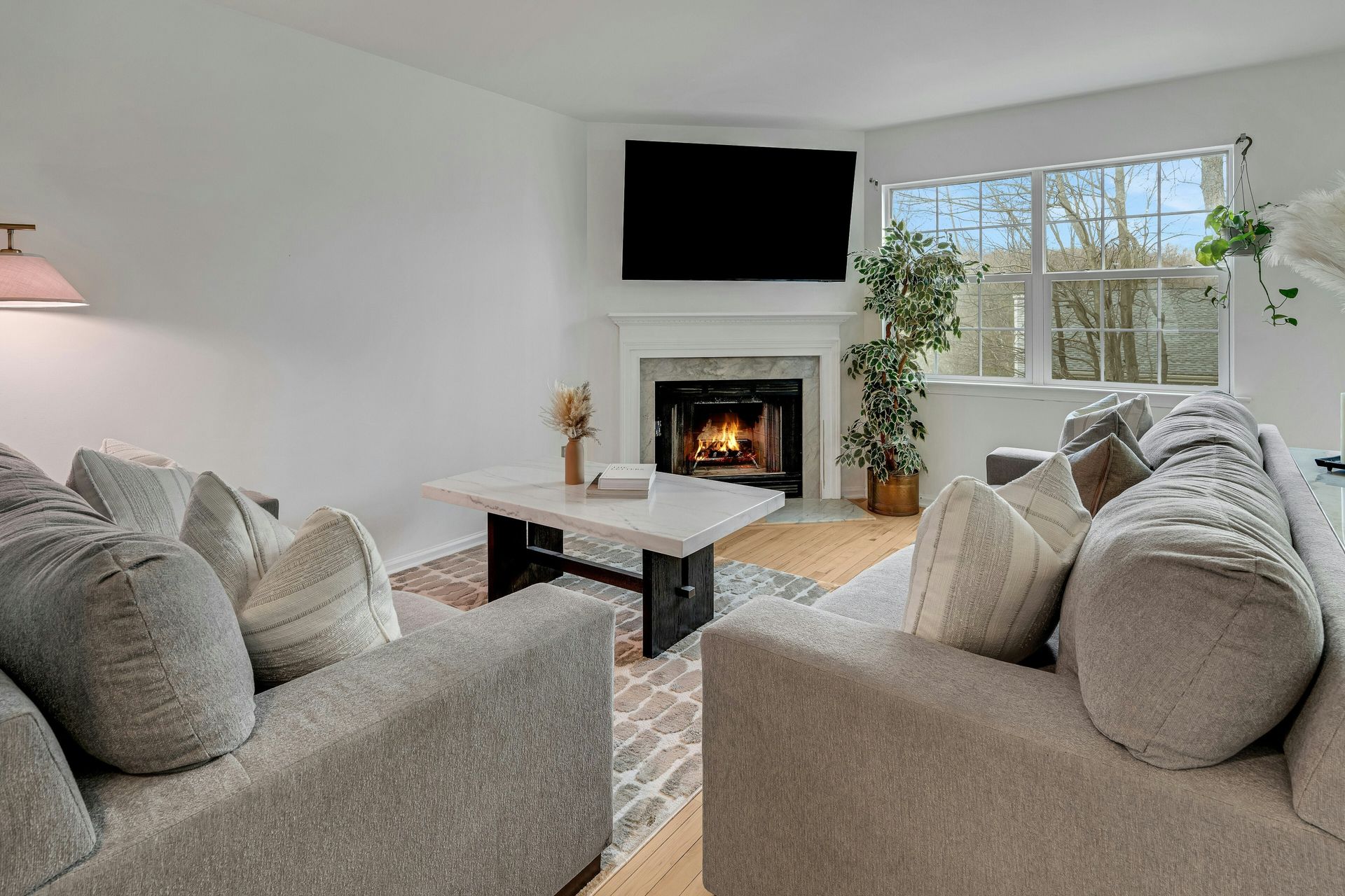 Cozy living room with gray sofas, fireplace, and large TV above it, brightened by natural light.