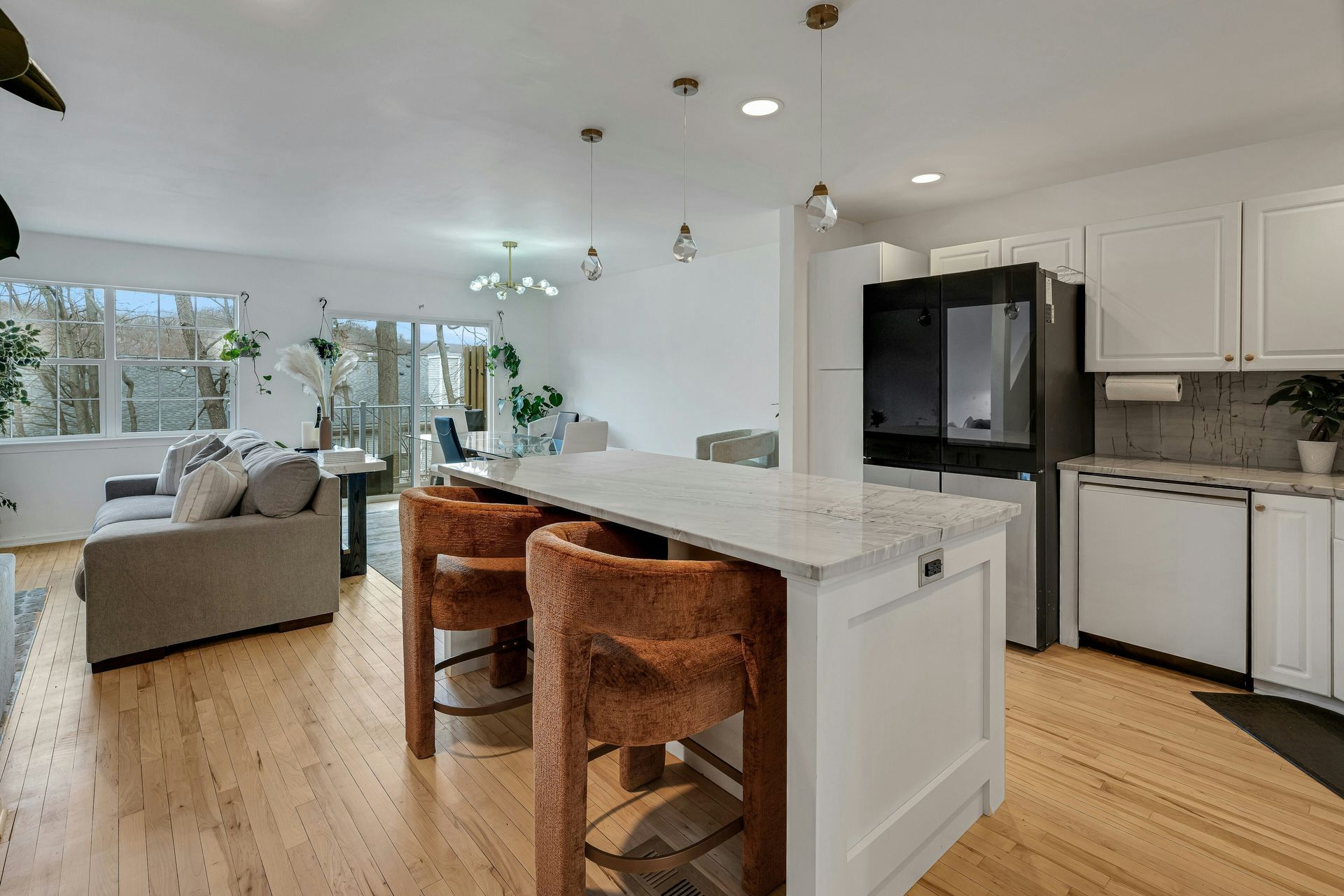 Open-concept kitchen with white cabinets, island with brown stools, and a large refrigerator. Wooden floors throughout.
