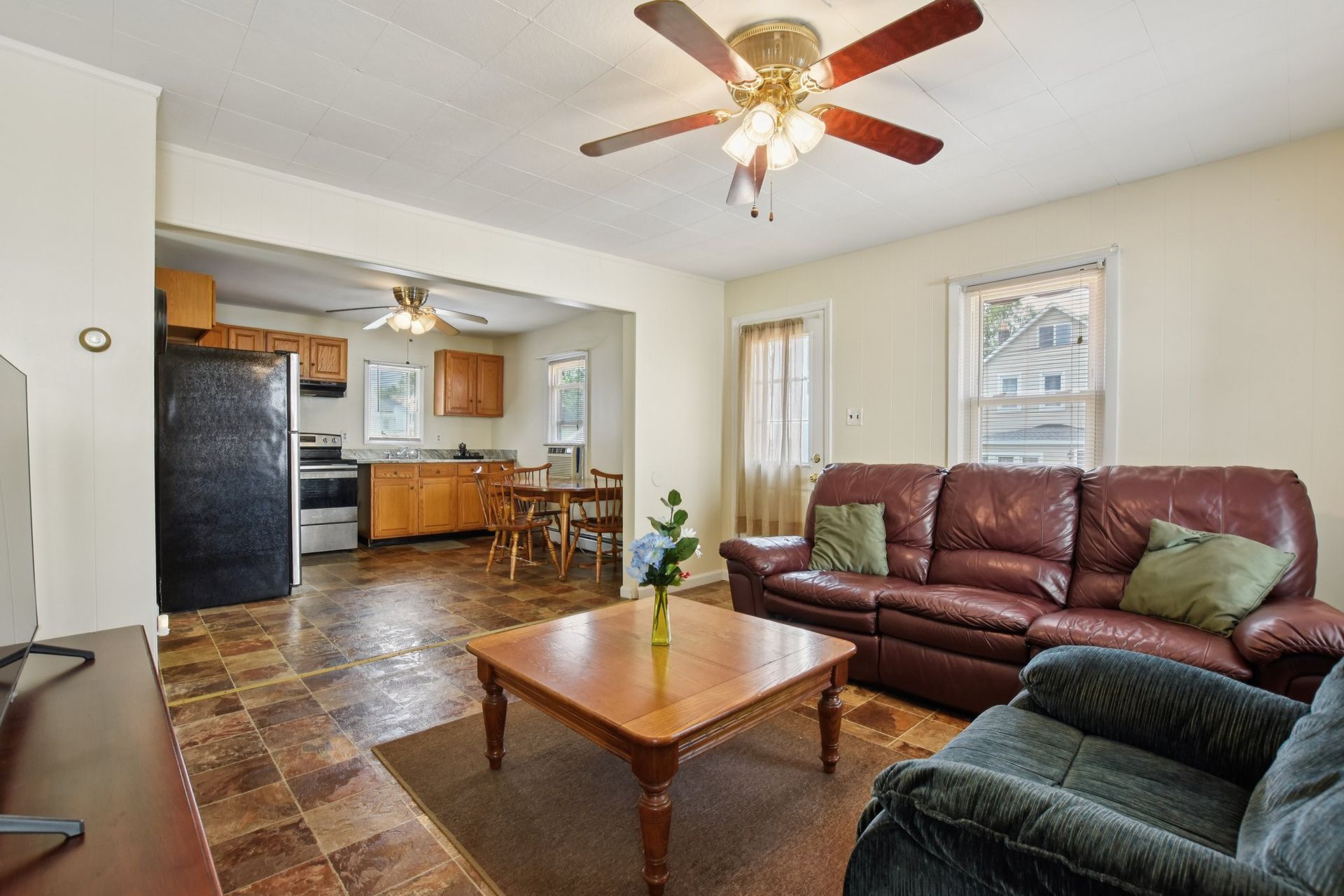 Living room with brown leather sofa, open to kitchen with wooden cabinets.