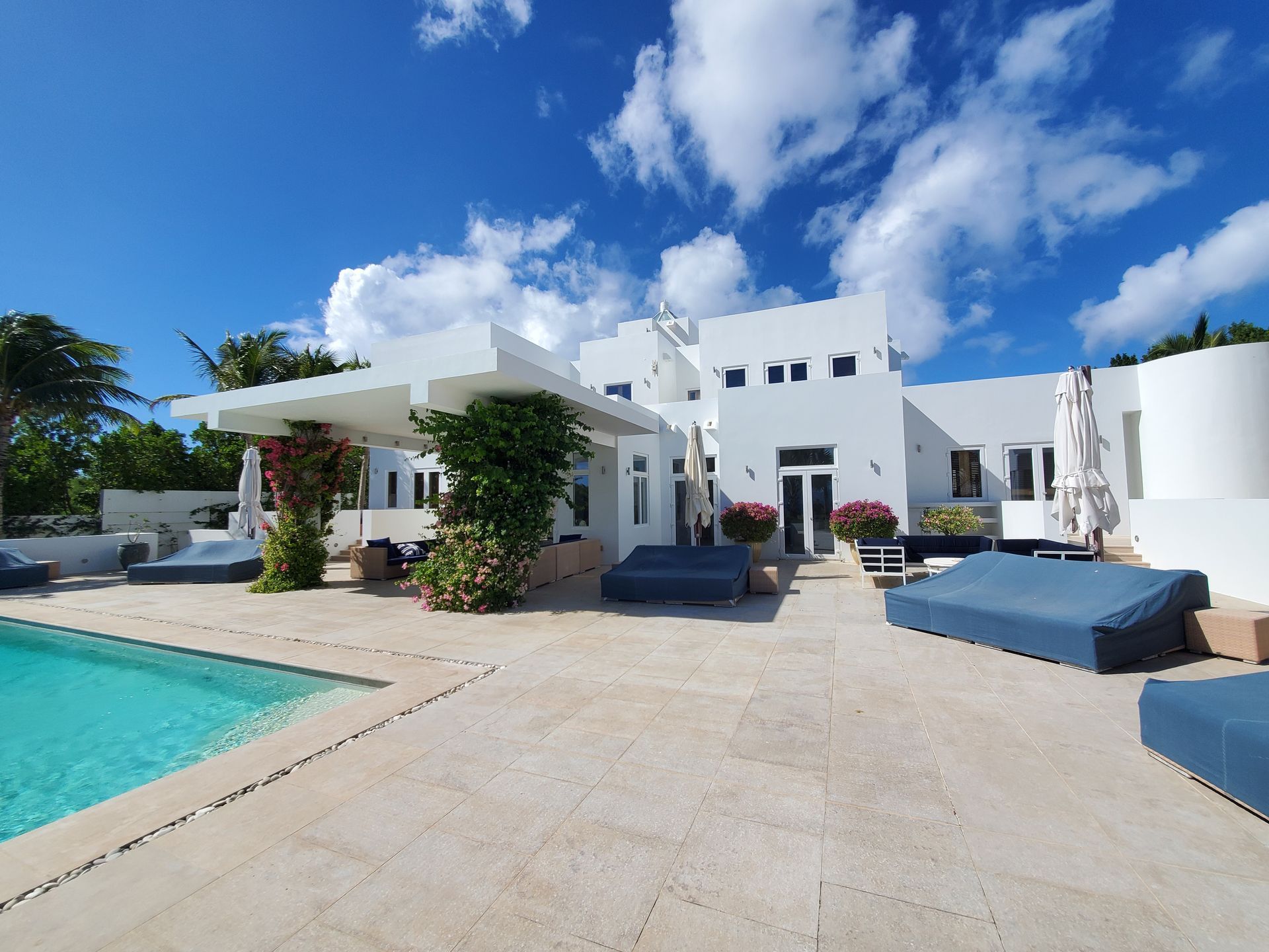White modern house with pool and lounge furniture under a bright blue sky.