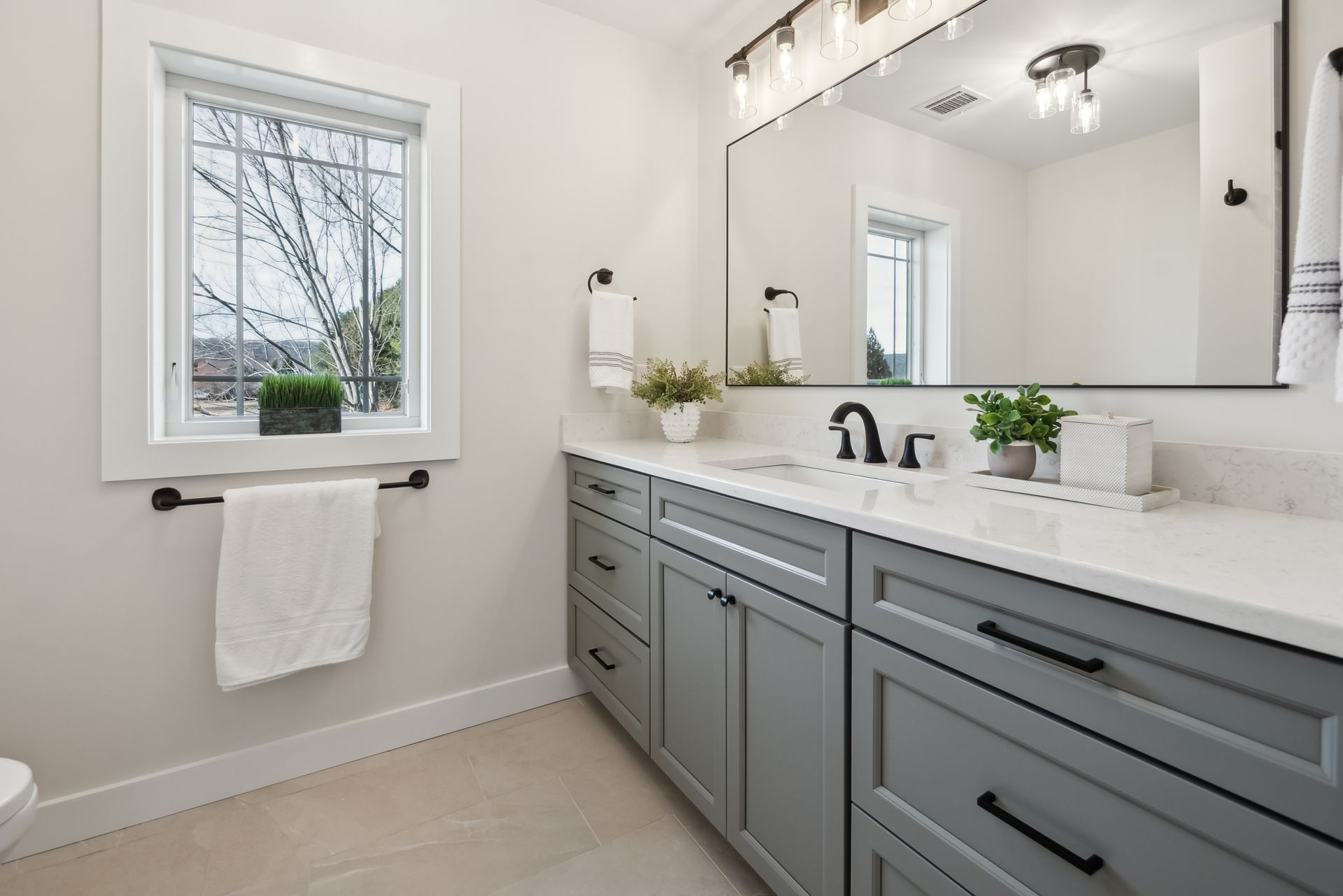 Bathroom with gray vanity, white countertop, large mirror, window, and neutral walls.
