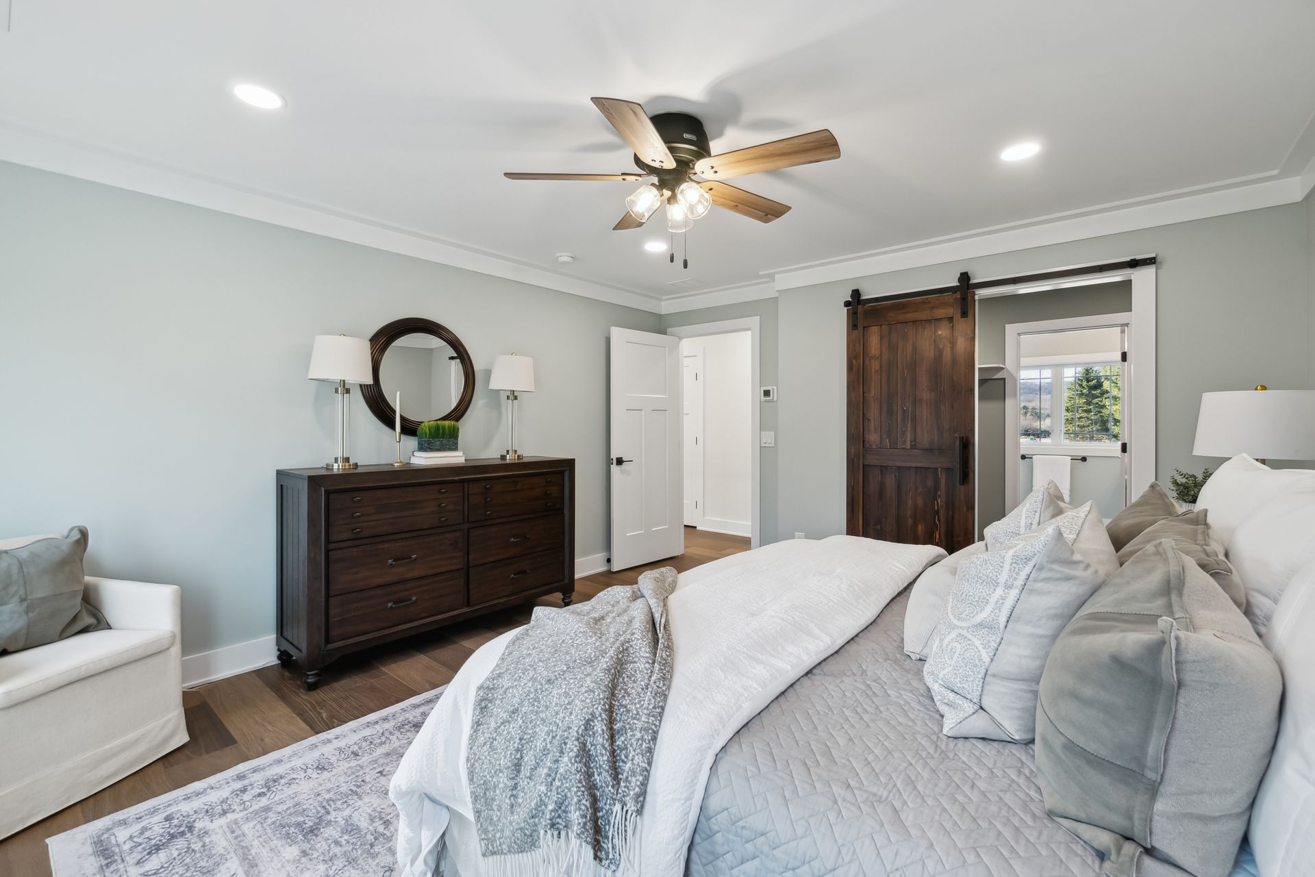 Bedroom with a bed, dresser, barn door, light blue walls, and a ceiling fan.