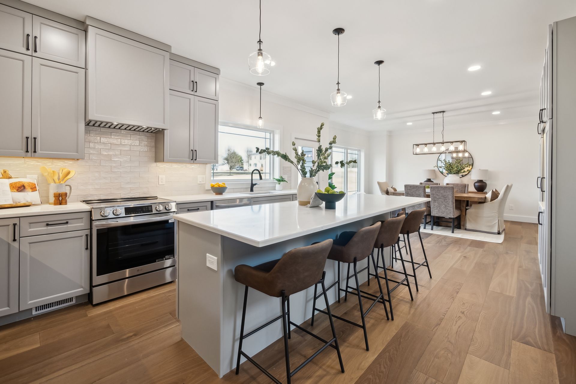 Modern kitchen with gray cabinets, white countertops, and wood flooring; island with bar stools.