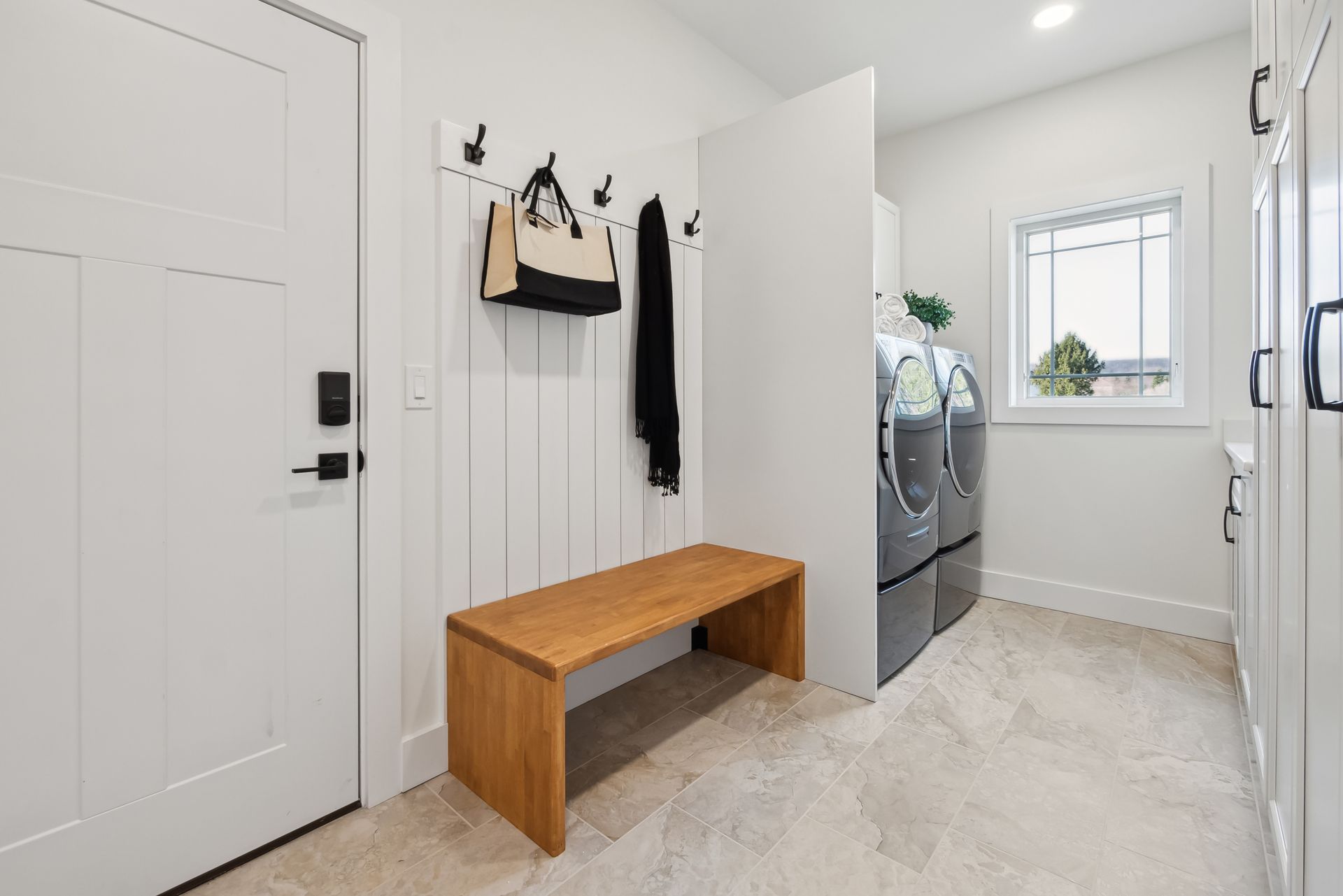 Laundry room with white walls, wood bench, and washer/dryer.