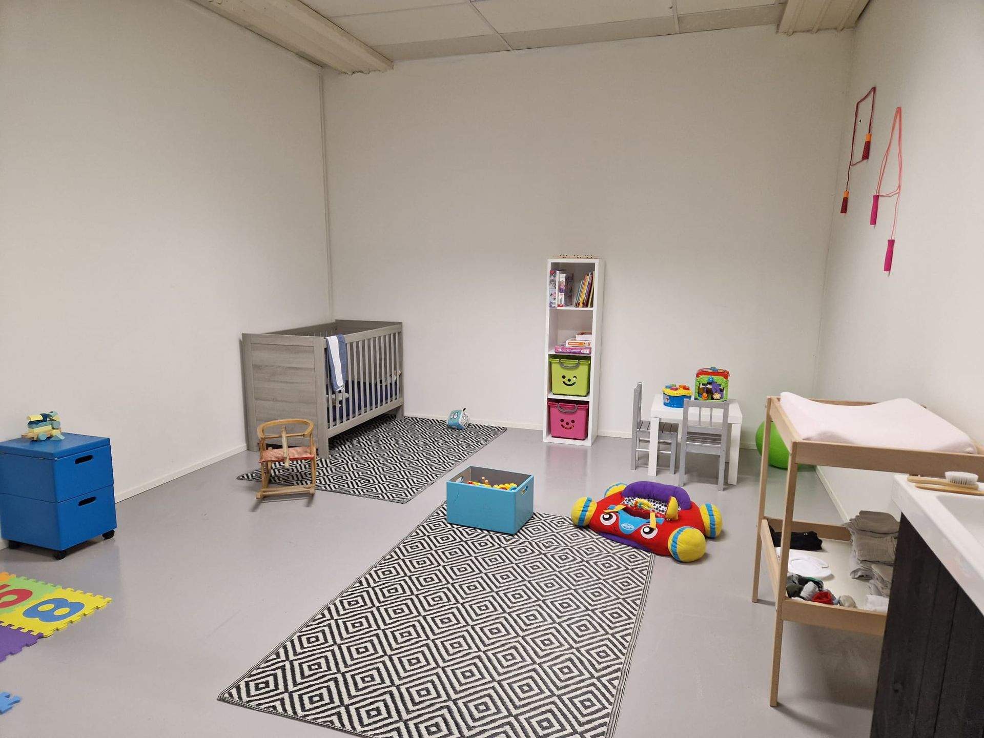 Een kamer met een wieg, tafel, stoelen en een vloerkleed.