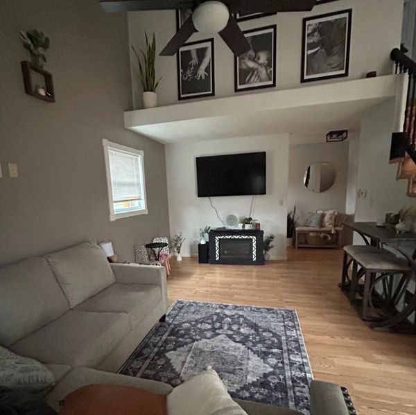 Cozy living room with gray sofa, wall-mounted TV, fireplace, rug, and lofted wall art.
