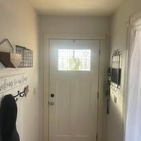 Narrow entryway with white front door, wall decor, and a black coat hanging on the left wall.