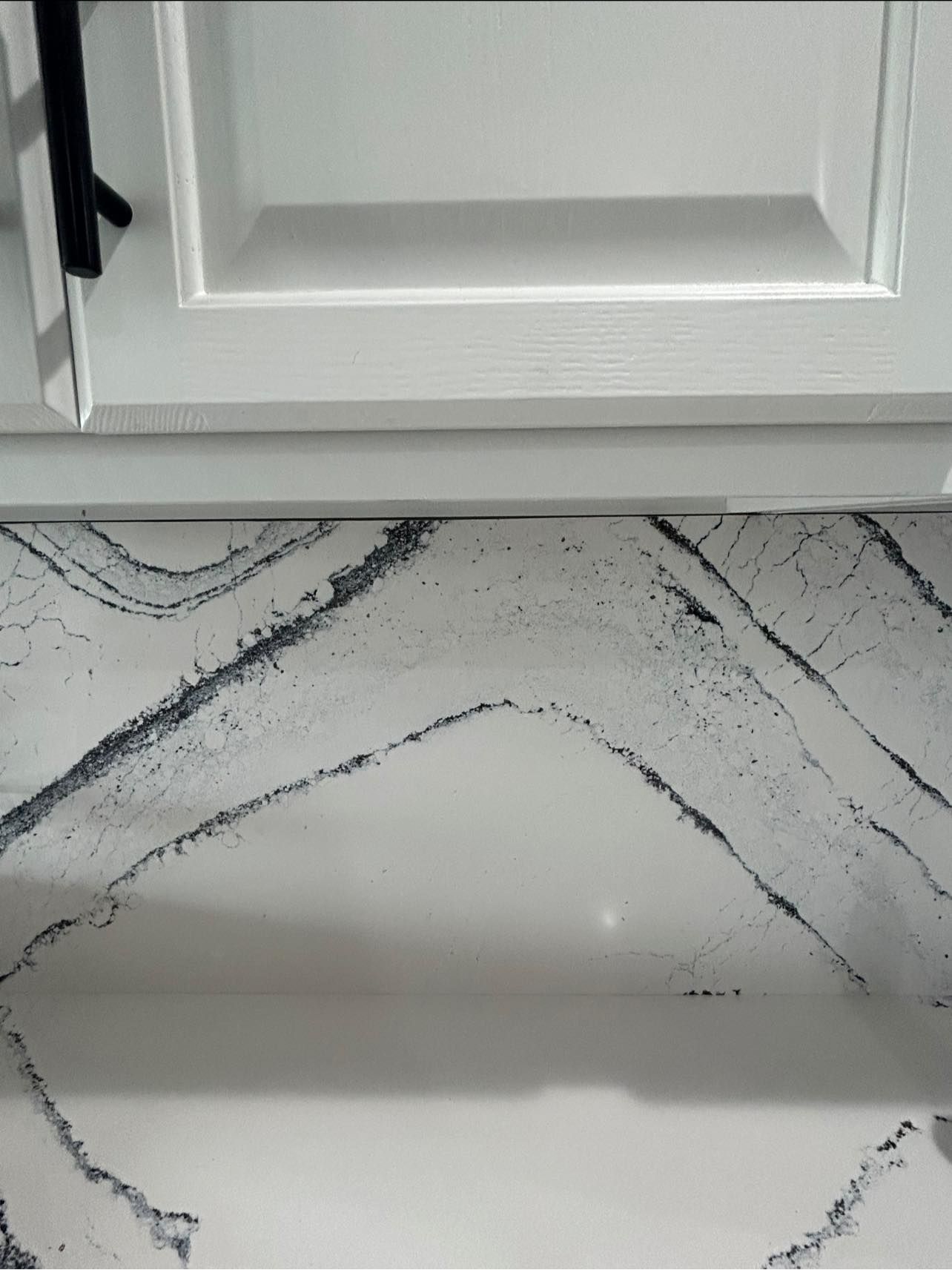 White kitchen cabinet above a marble-patterned tile backsplash and countertop