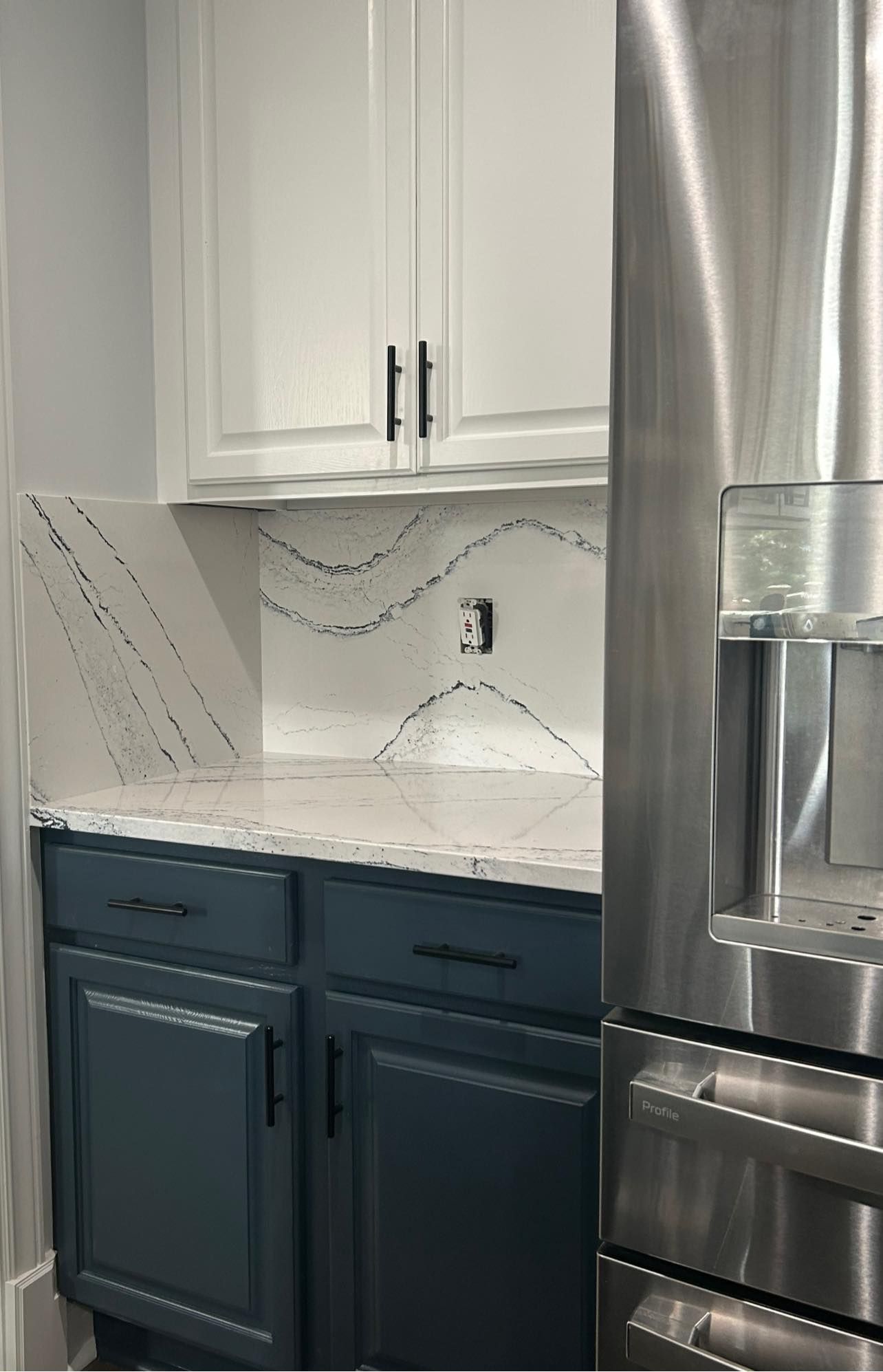 Modern kitchen with dark blue cabinets, white countertops, and a stainless steel refrigerator