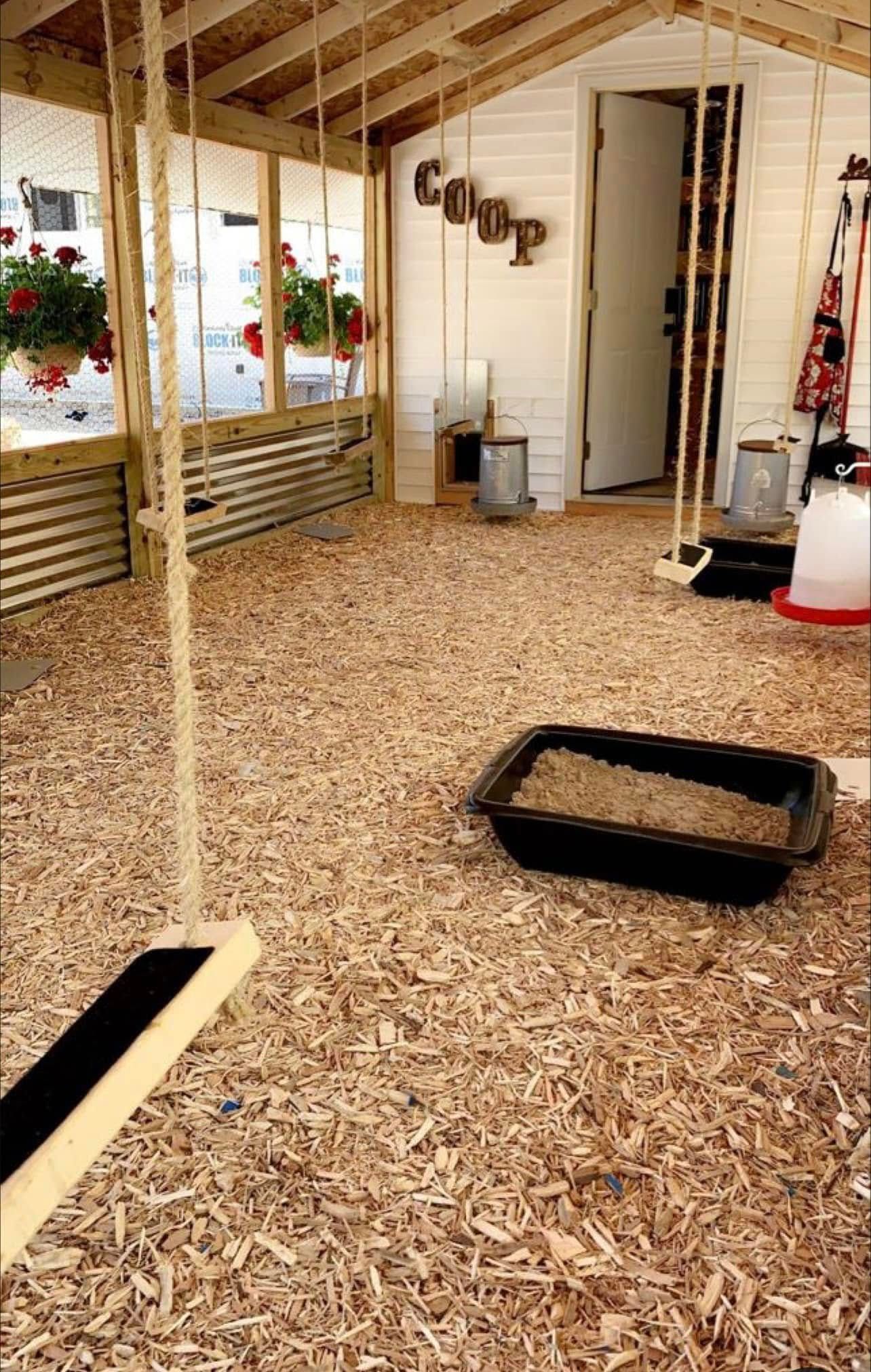 Empty chicken coop with wood shavings, nesting boxes, and a black tray on the floor.