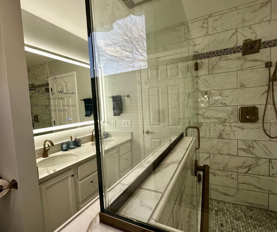 Modern bathroom with vanity, large mirror, glass shower, marble tile, and a shower bench
