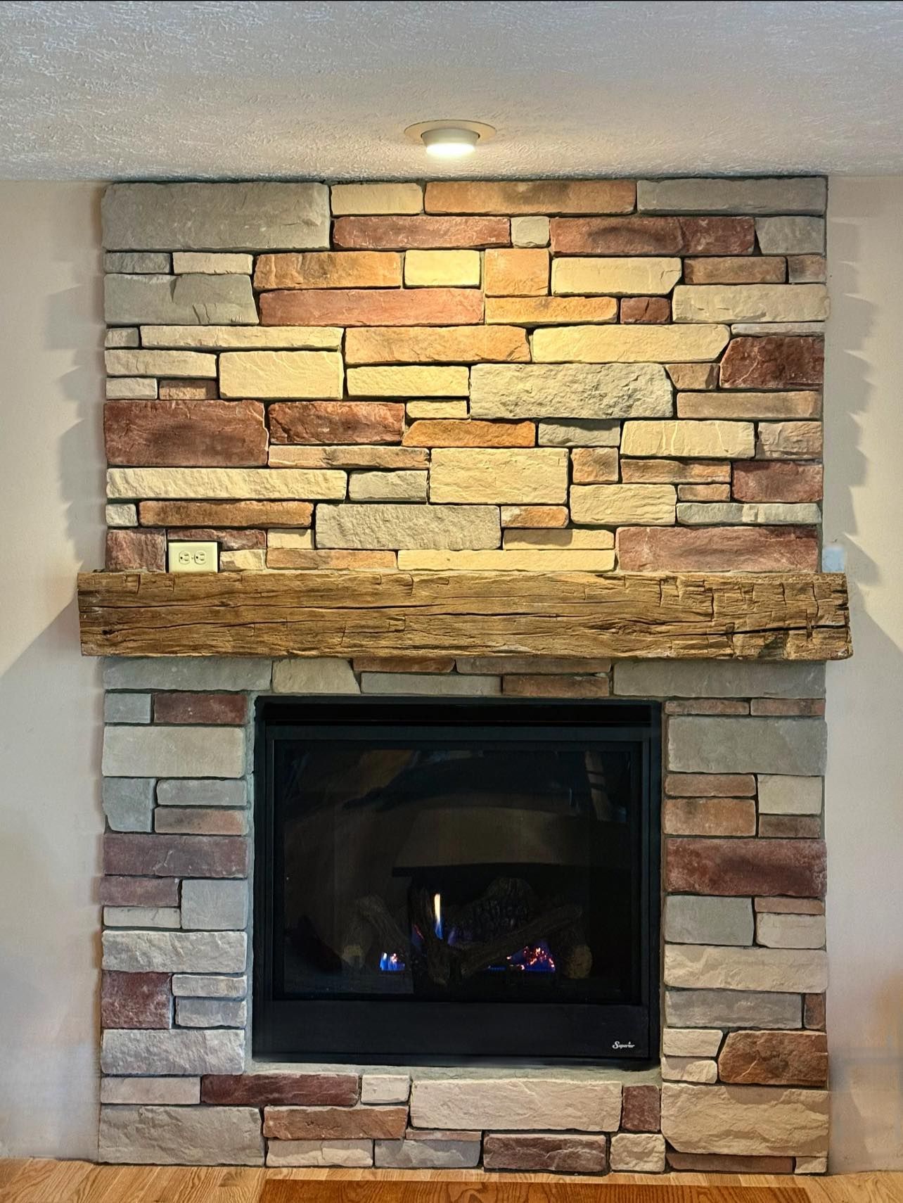 Stone fireplace with a dark glass firebox and a wood mantel under a lit wall sconce
