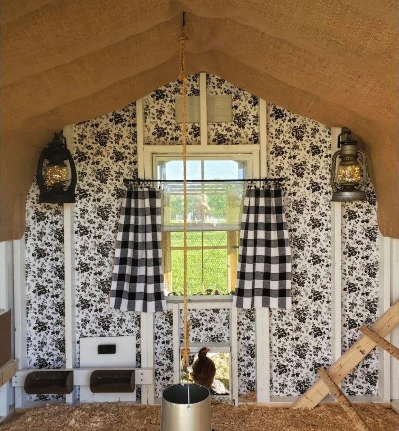 Small attic room with floral wallpaper, checkered curtains, hanging lanterns, and a cat by the window.