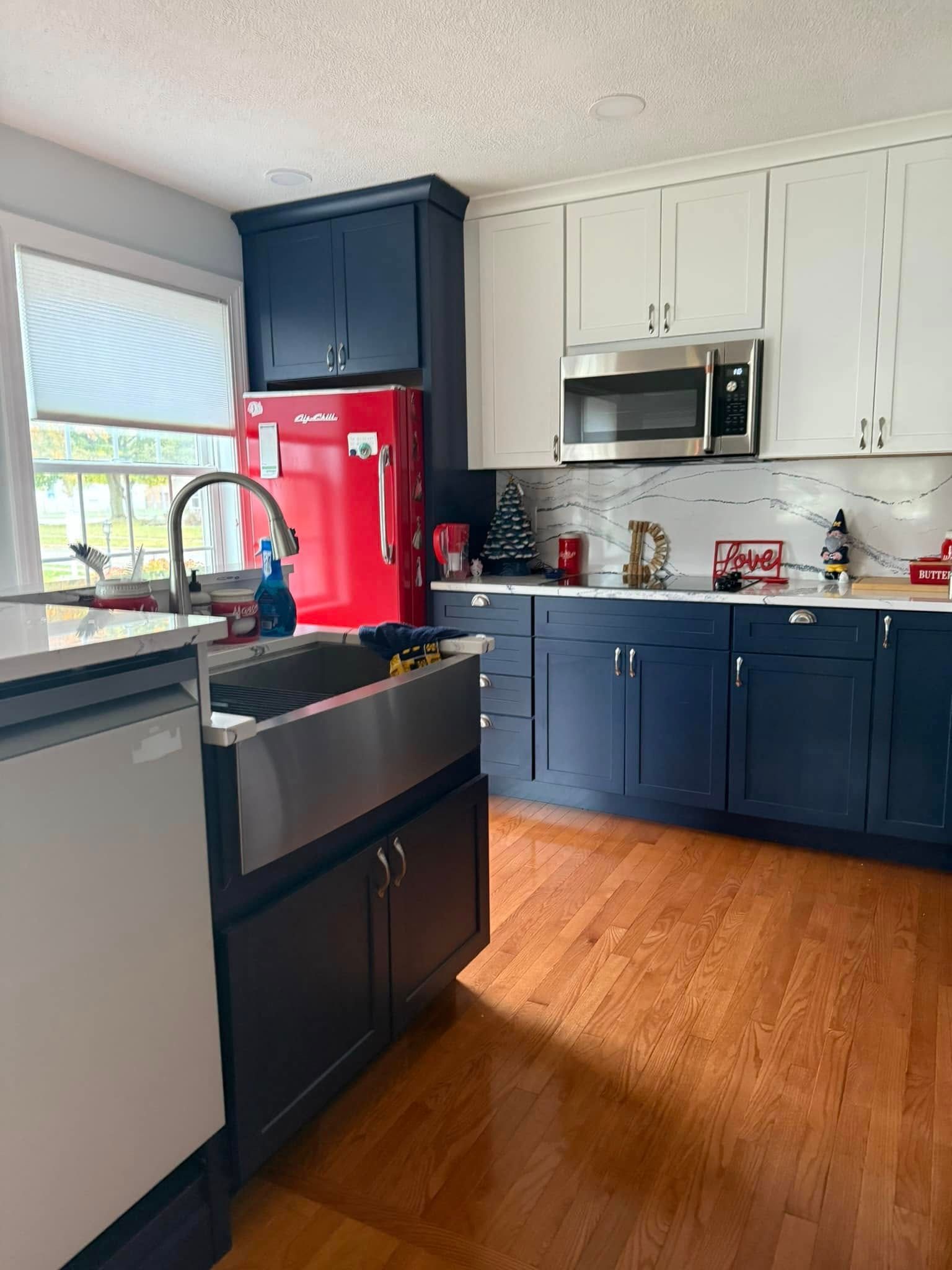 Modern kitchen with navy and white cabinets, red refrigerator, black stove, and wood floors