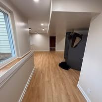 Narrow empty hallway with wood floor, white walls, windows, and a coat rack near the end.