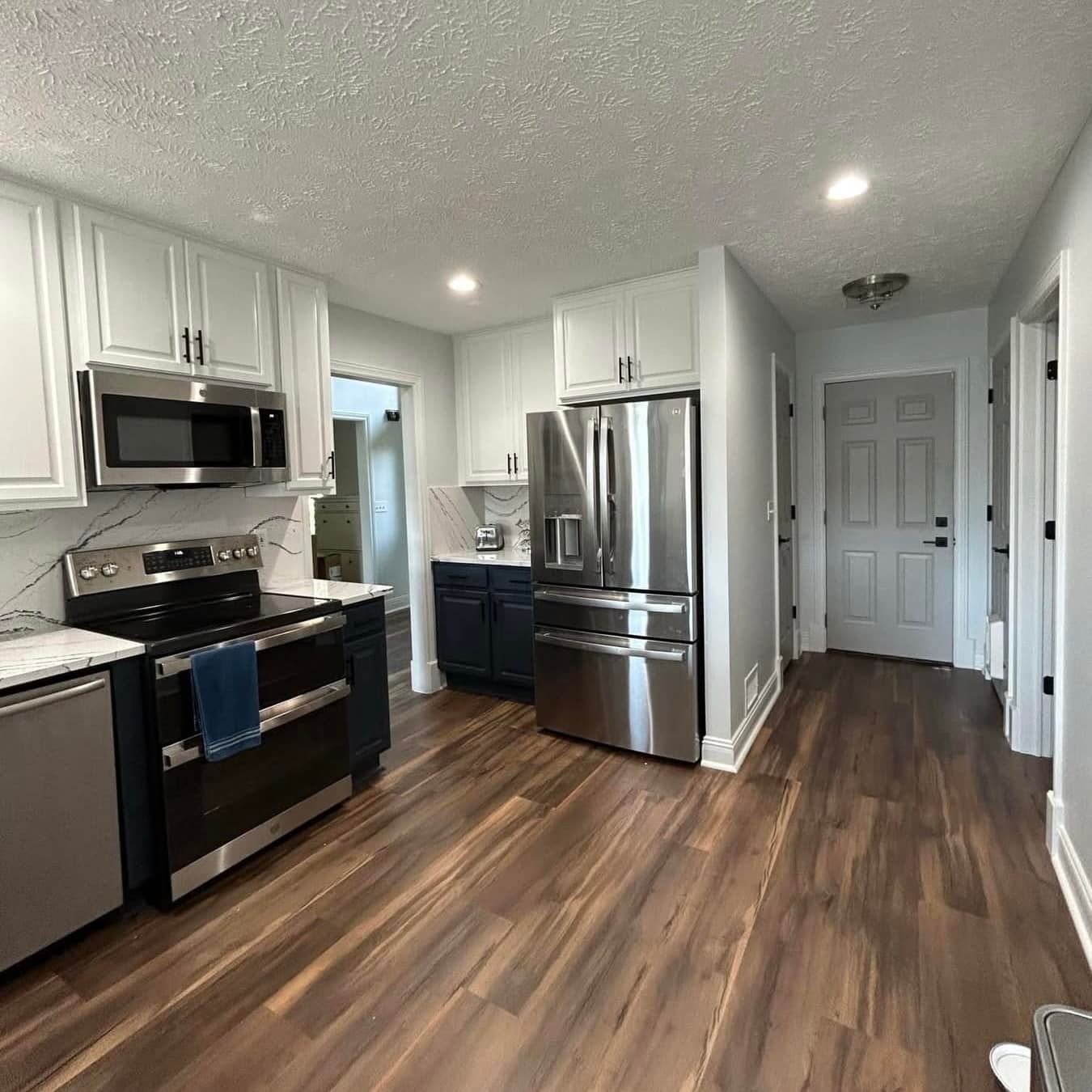 Modern kitchen with stainless steel appliances, white cabinets, and wood-look flooring