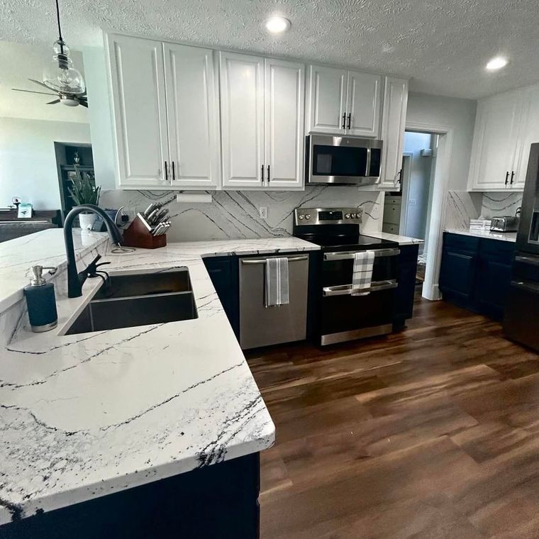 Modern kitchen with white cabinets, black appliances, marble counters, and wood flooring