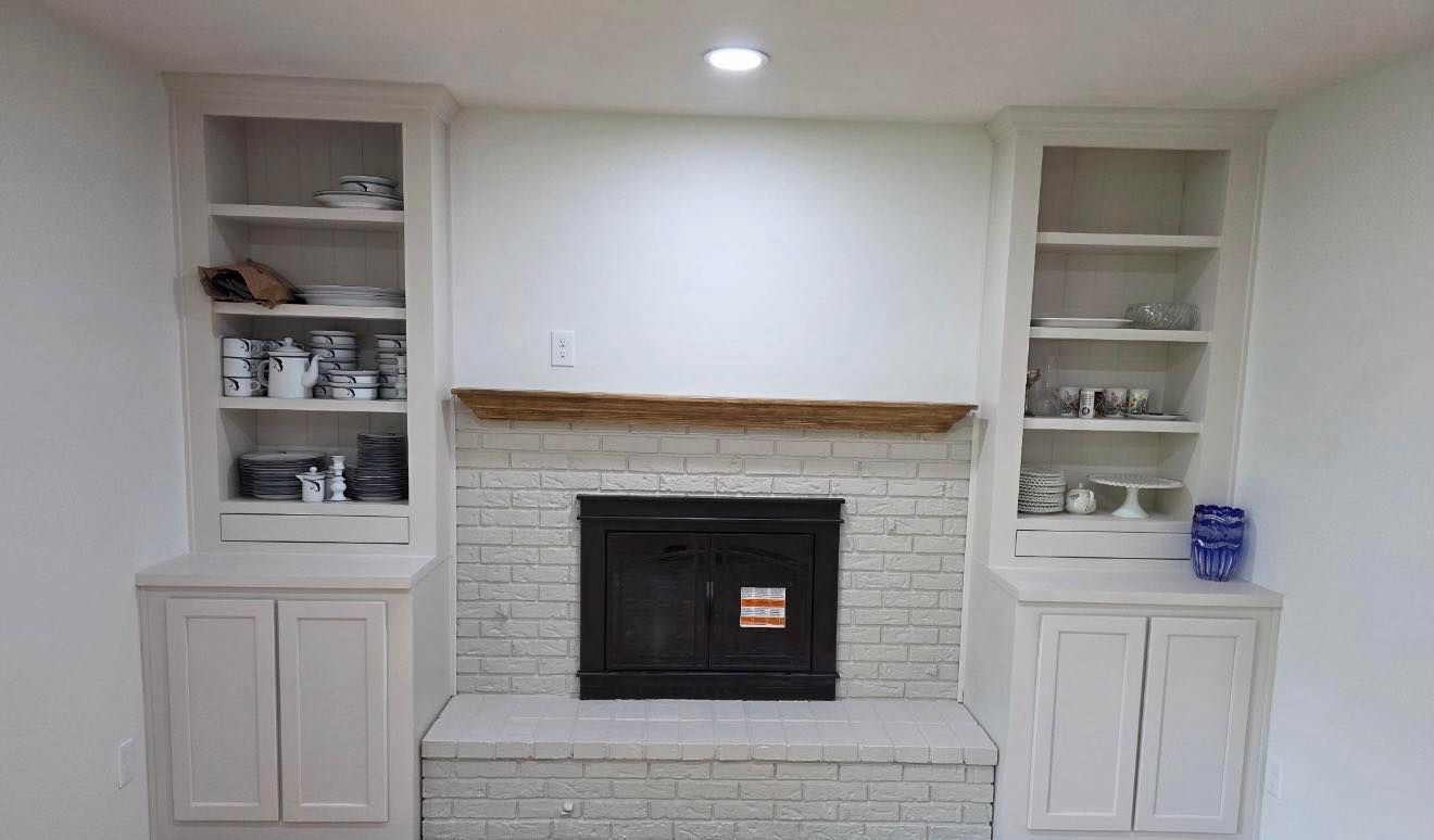 White living room with a brick fireplace, built-in shelves, and cabinet storage on both sides