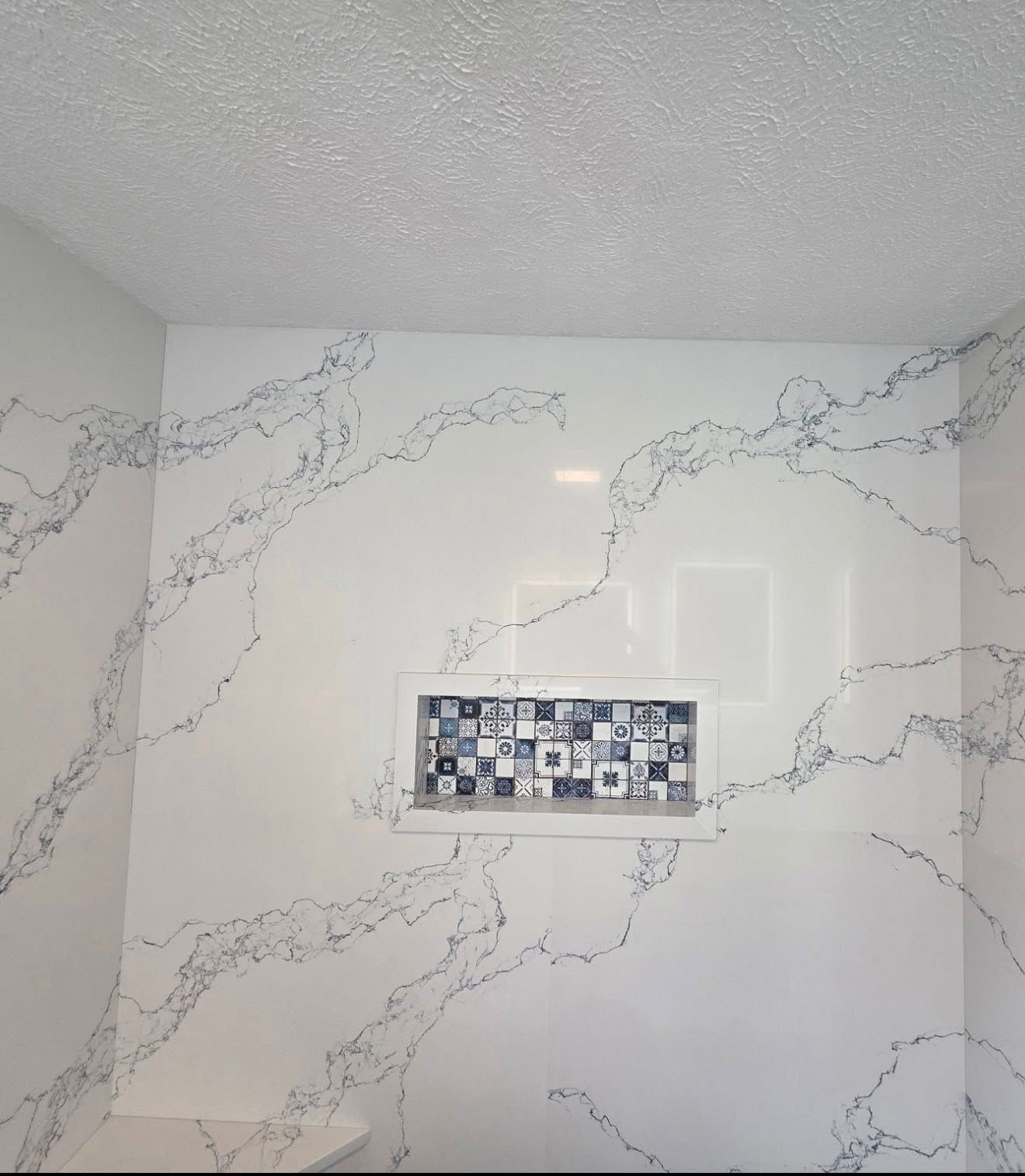 Bathroom wall with white marble-look tile and a small decorative mosaic accent strip