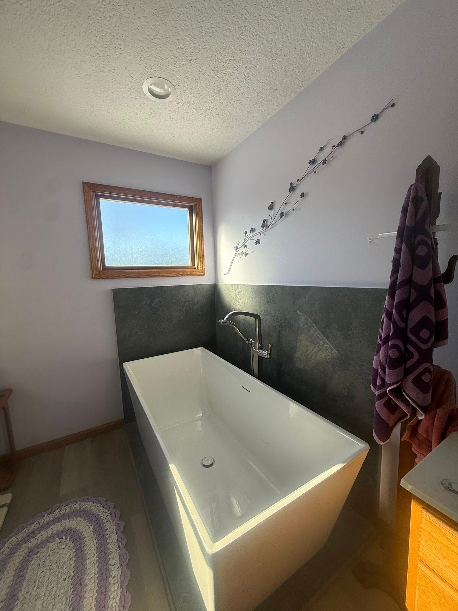 Bathroom with a white soaking tub, gray half-wall, small window, and towel hanging on the right.