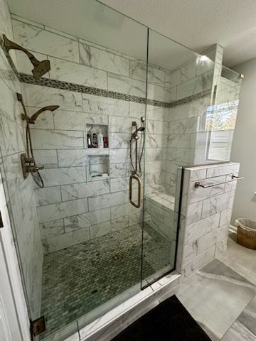 Bathroom with two sinks, gray tile, large mirrors, white towels, and open storage.