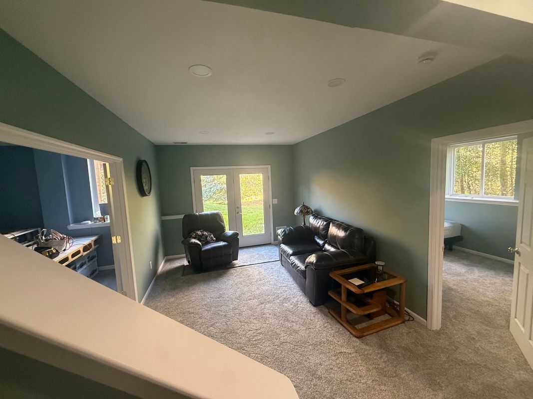Spacious living room with green walls, two dark sofas, and a doorway to a sunlit bedroom.