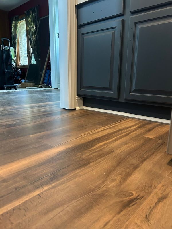 Kitchen floor with wood-grain laminate and dark gray cabinets near a hallway.