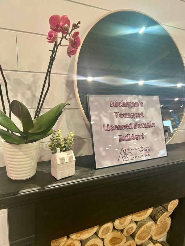 Welcoming sign beside pink orchid and blue mirror on a black shelf over decorative logs