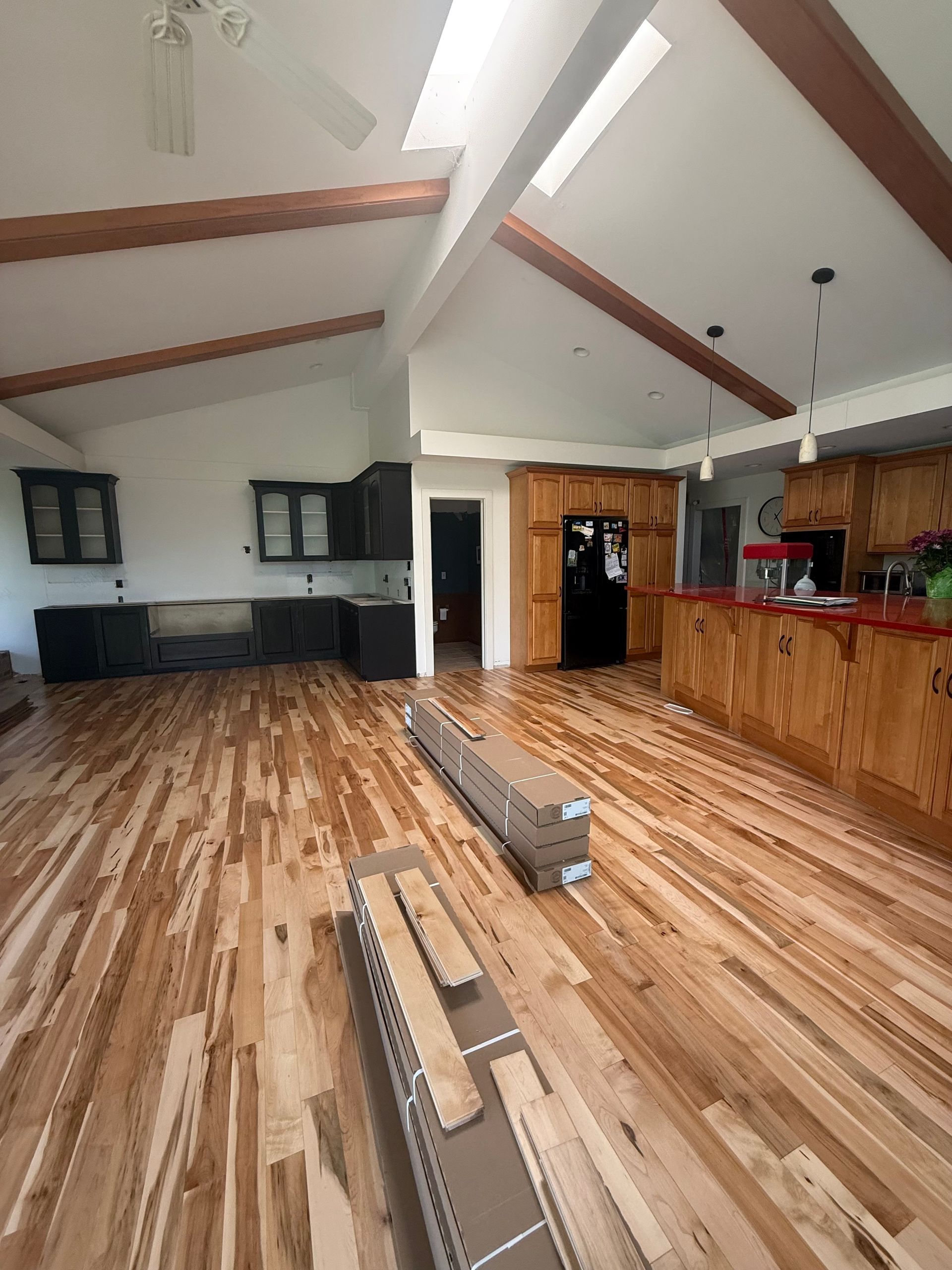 Open-concept kitchen and living area with wood floors, exposed beams, and dark cabinets.