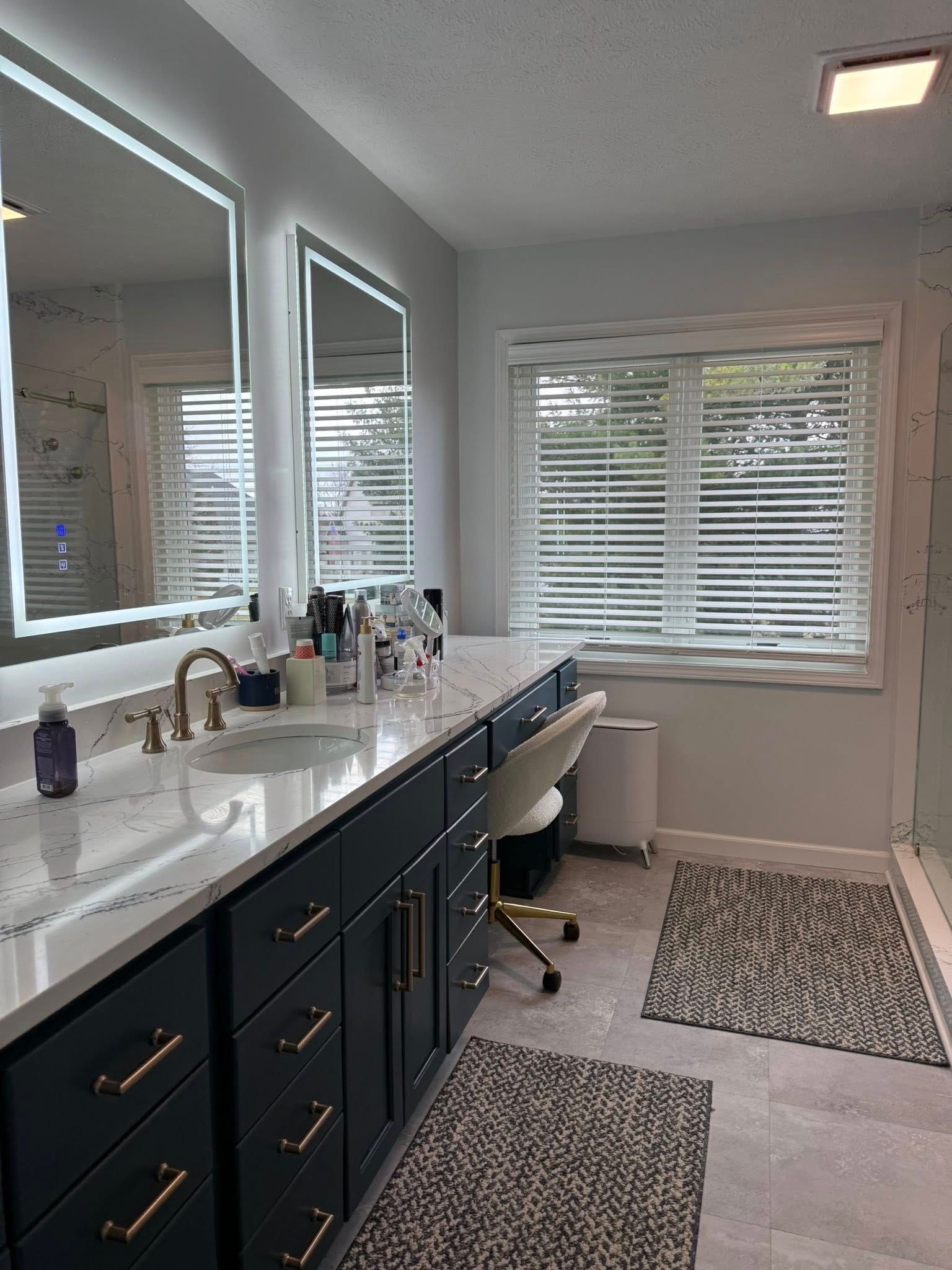 Modern bathroom with a double vanity, mirror, window blinds, and patterned rugs