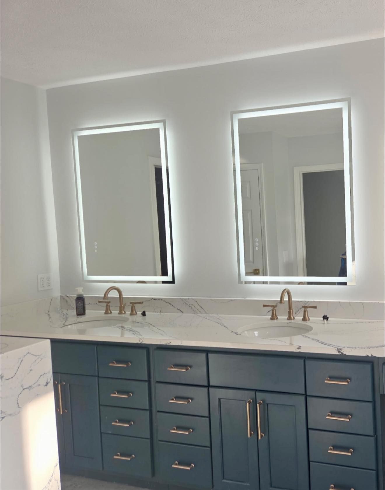 Modern bathroom vanity with blue cabinets, double mirrors, and brass faucets against a light gray wall