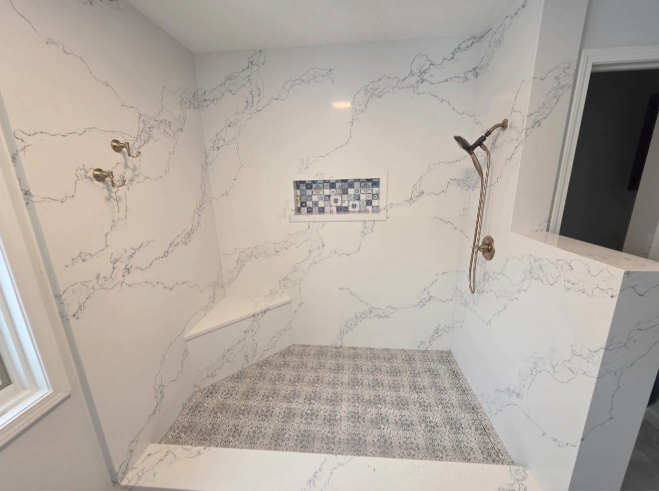 White marble-look shower with a built-in bench, small tile accent shelf, and window on the left.