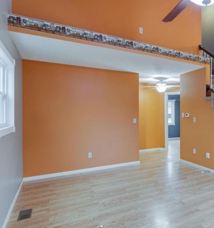 Empty room with orange walls, light wood flooring, white trim, and a doorway in the back.