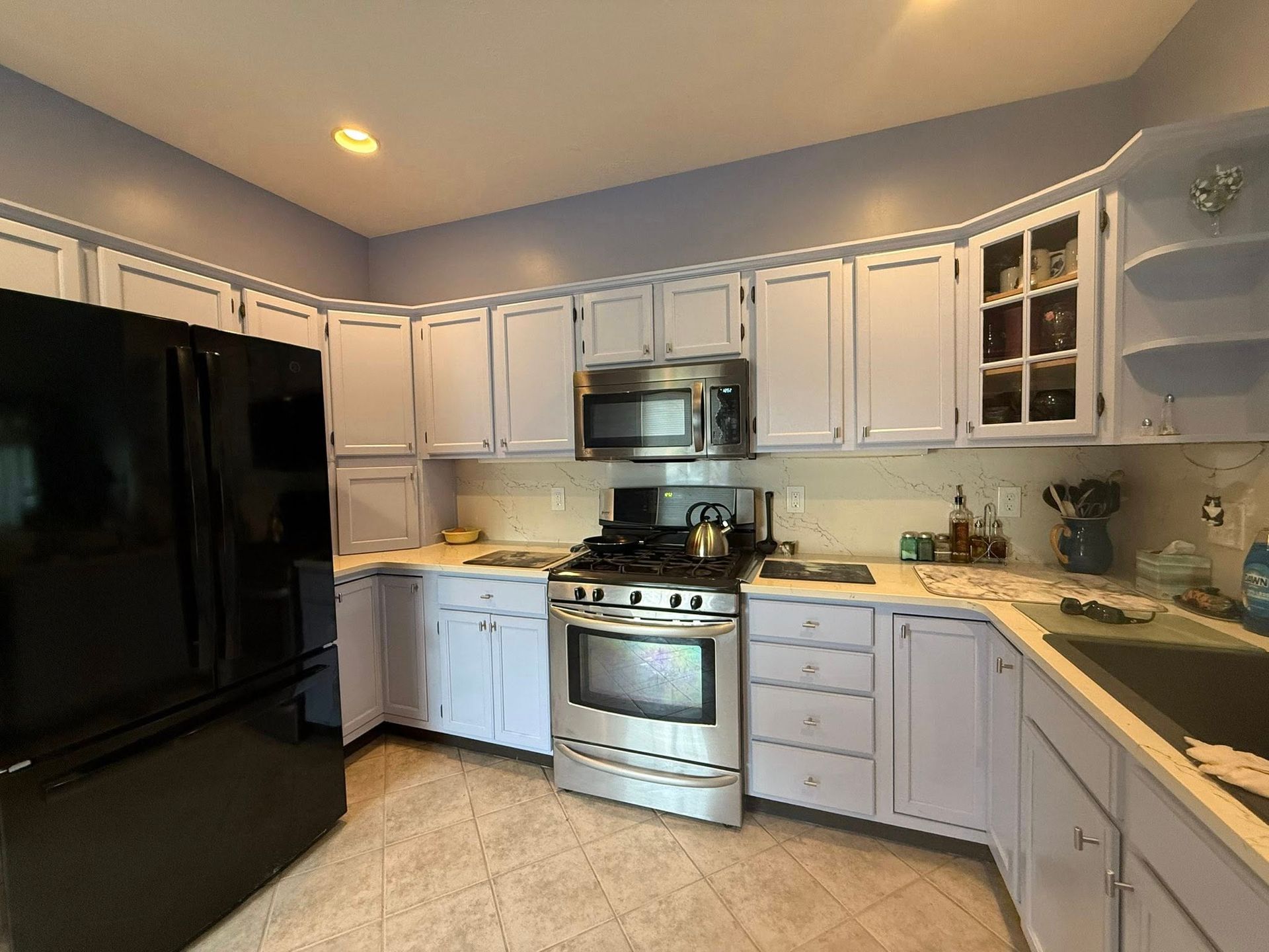 Bright kitchen with white cabinets, black fridge, stainless stove, and beige tile floor