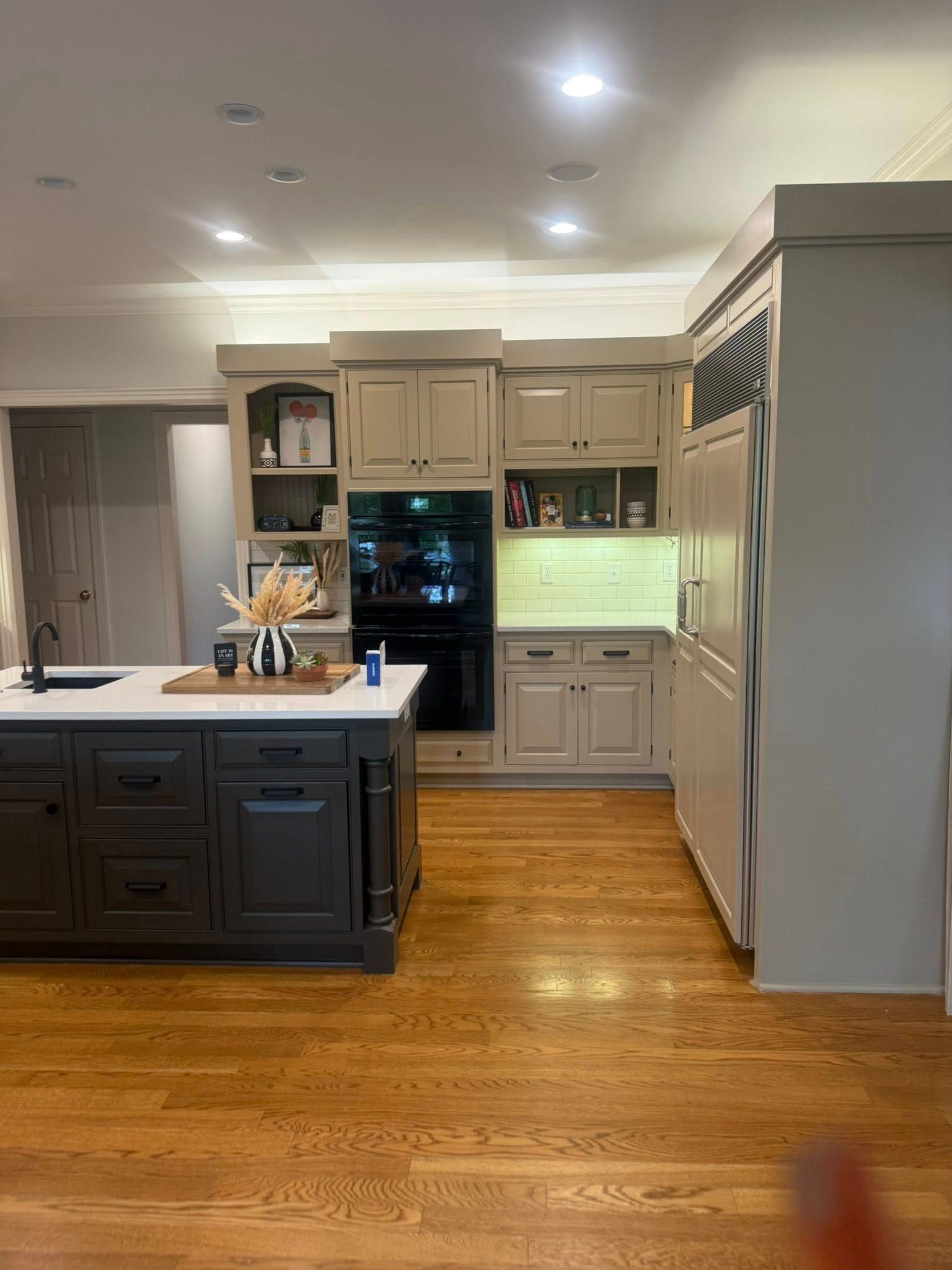 Modern kitchen with two-tone island, beige cabinets, hardwood floors, and built-in oven and microwave.