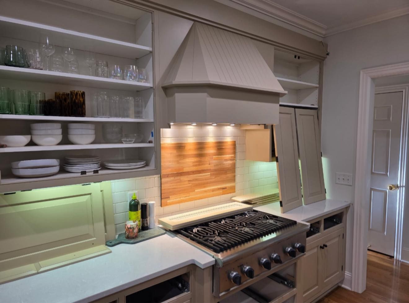 Bright kitchen with white cabinets, gas range, wood backsplash, and open shelving with dishes