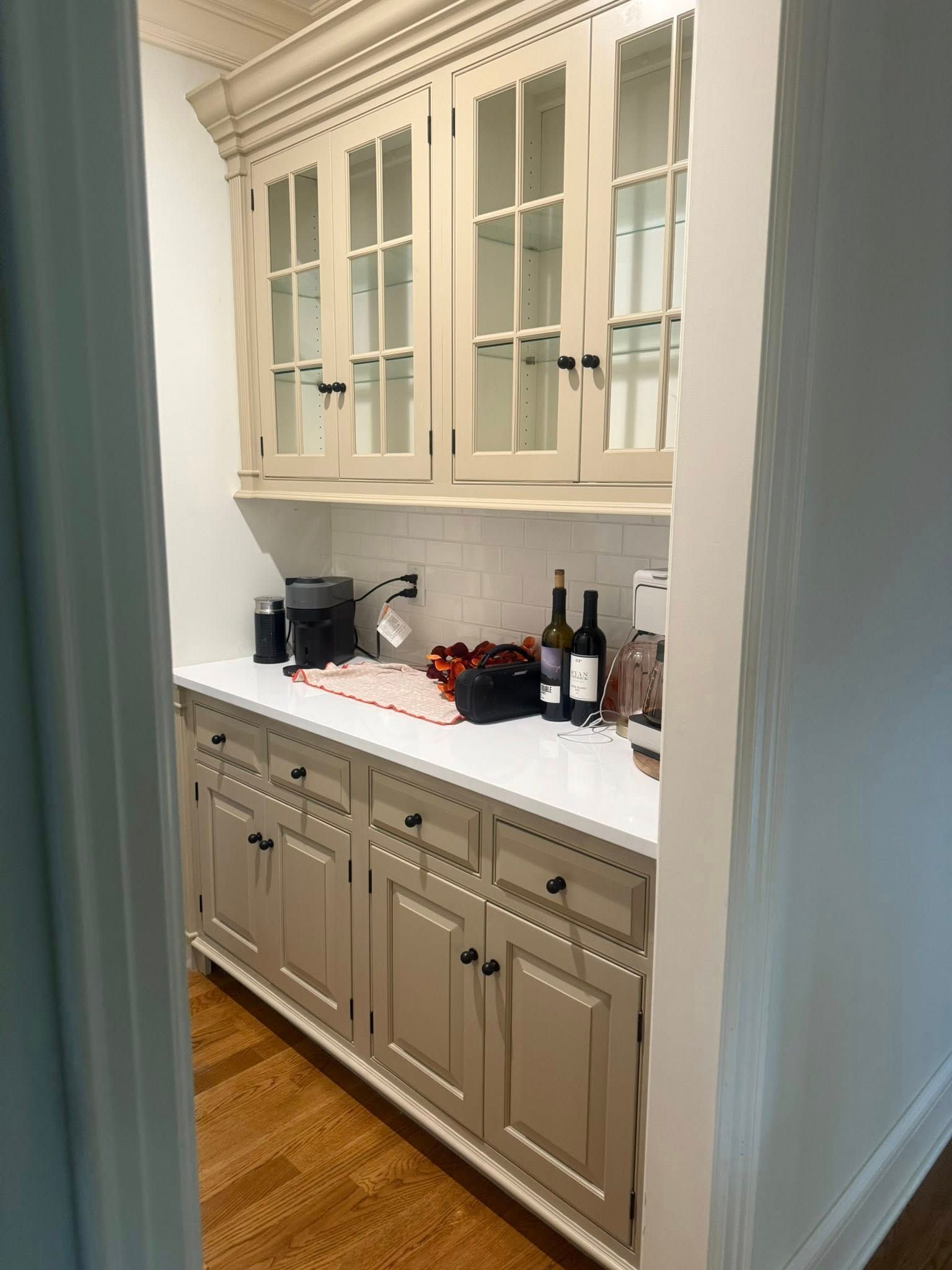 Built-in kitchen cabinet with white glass-front uppers, gray lowers, and countertop appliances and bottles