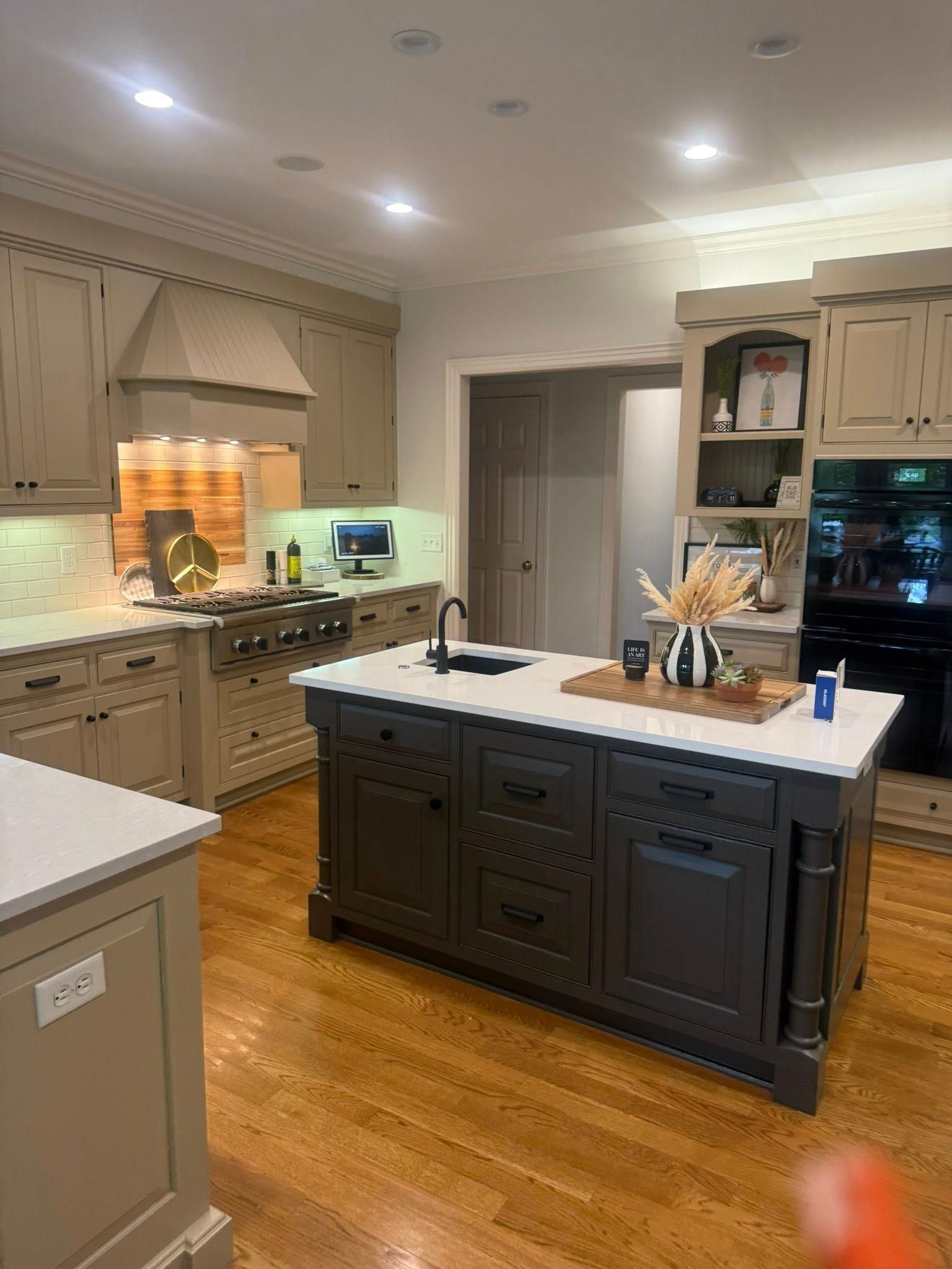 Bright kitchen with dark island, white countertops, wood floors, and built-in cabinets around the room