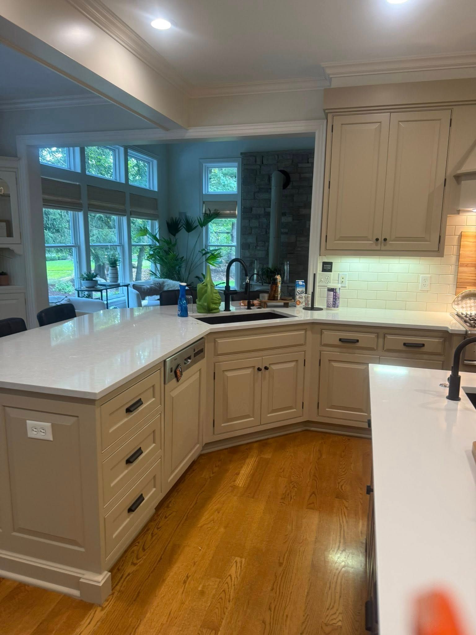 Bright kitchen with beige cabinets, white countertops, hardwood floor, and large windows by the sink.