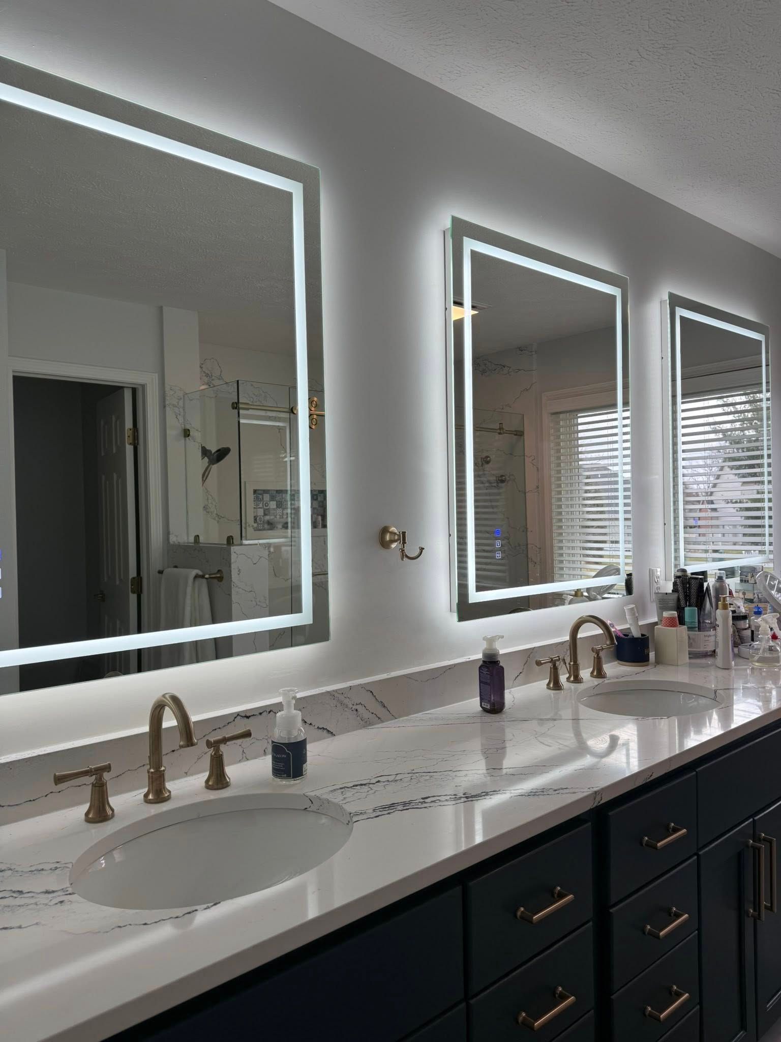 Modern bathroom vanity with double sinks, lit mirrors, brass faucets, and dark cabinets