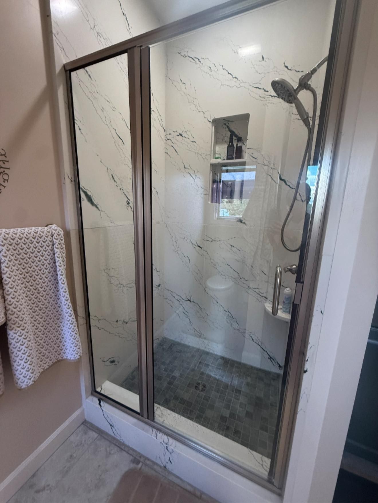 Glass shower stall with sliding doors and marble-pattern wall panels in a bathroom
