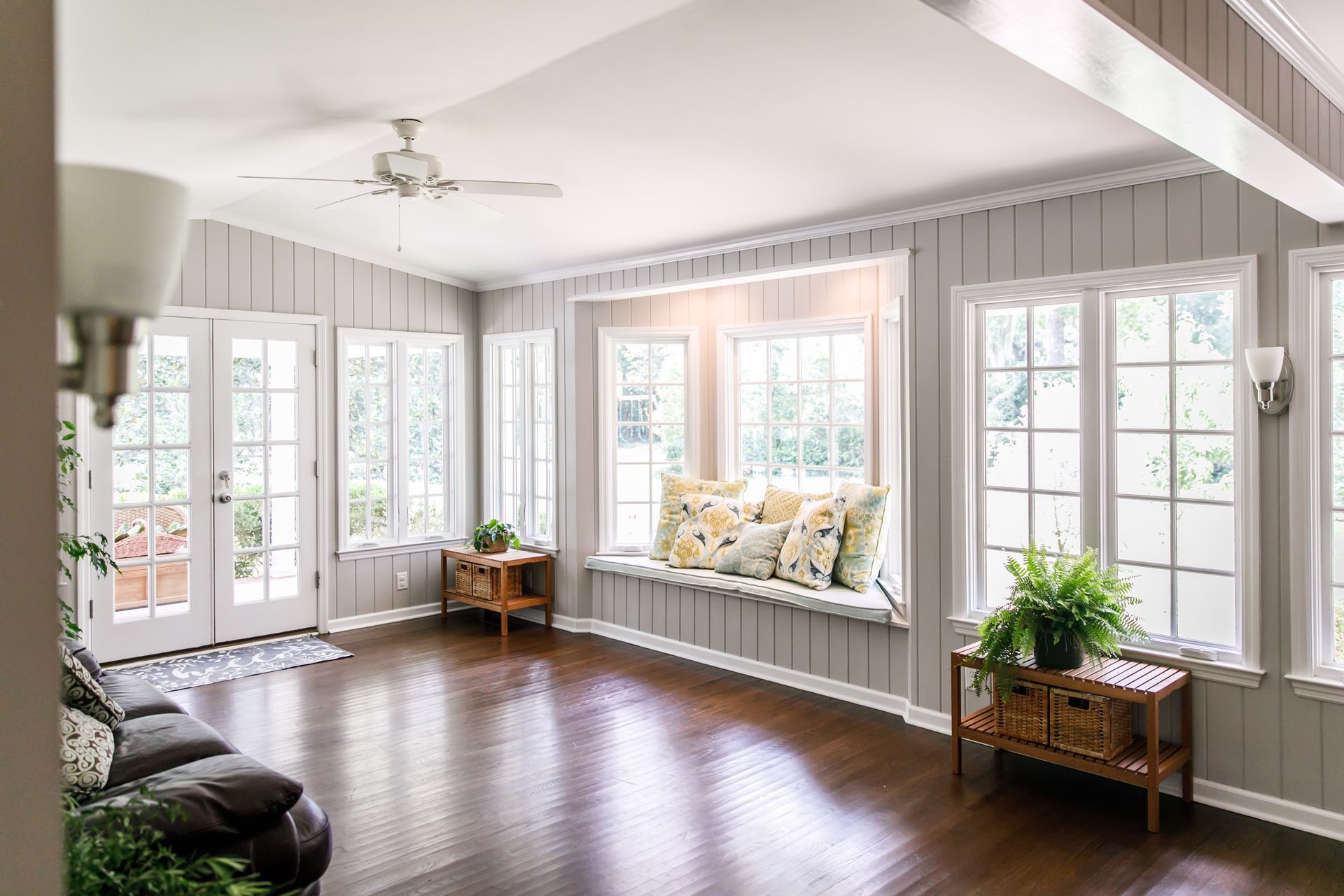 Sunroom with dark wood floors, gray walls, white trim, and a window seat with pillows.