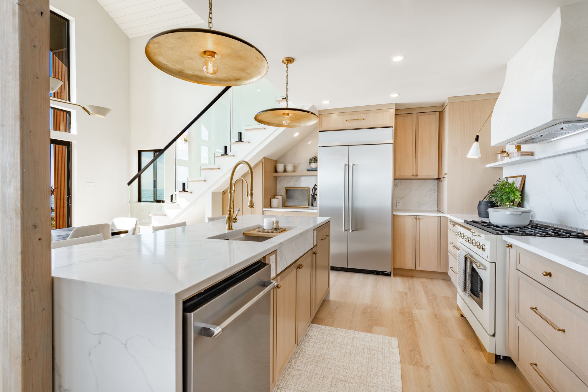 A bright, modern kitchen features light wood cabinets, white countertops, a large island, and stainless steel appliances.
