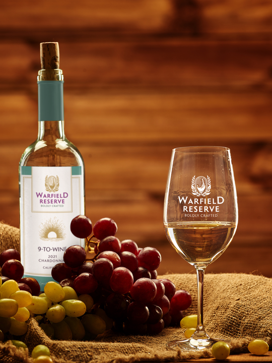 Bottle and glass of white wine with grapes, set against a wooden background.