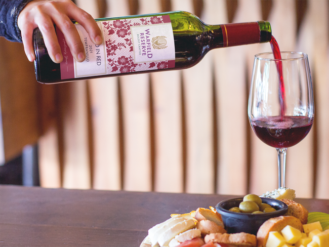 Person pouring red wine into a glass next to a cheese and cracker board.