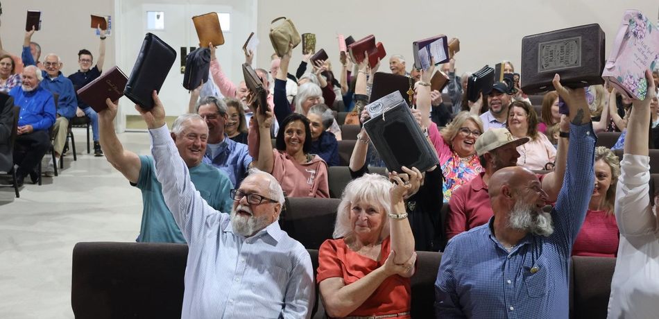 congregation smiling and holding up bibles 